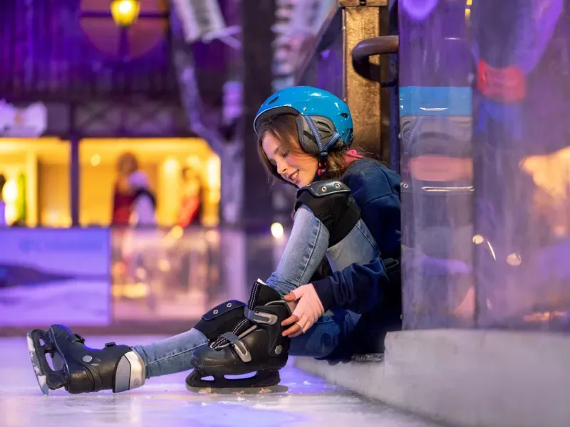 Menina calçando os patins em uma pista de patinação no gelo no parque snowland