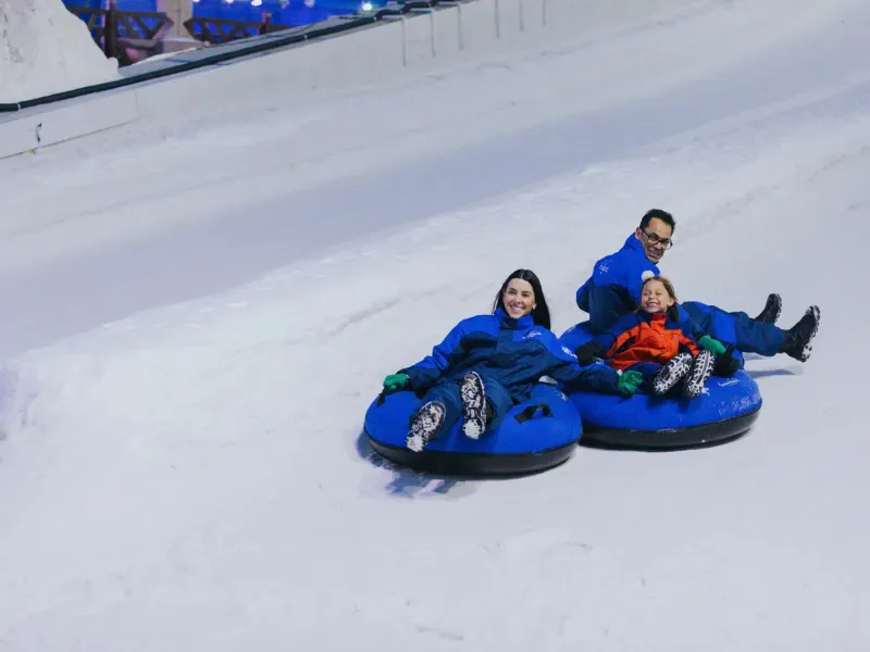 uma familia, formada por um pai, uma mãe e uma criança descendo de boias uma montanha de neve