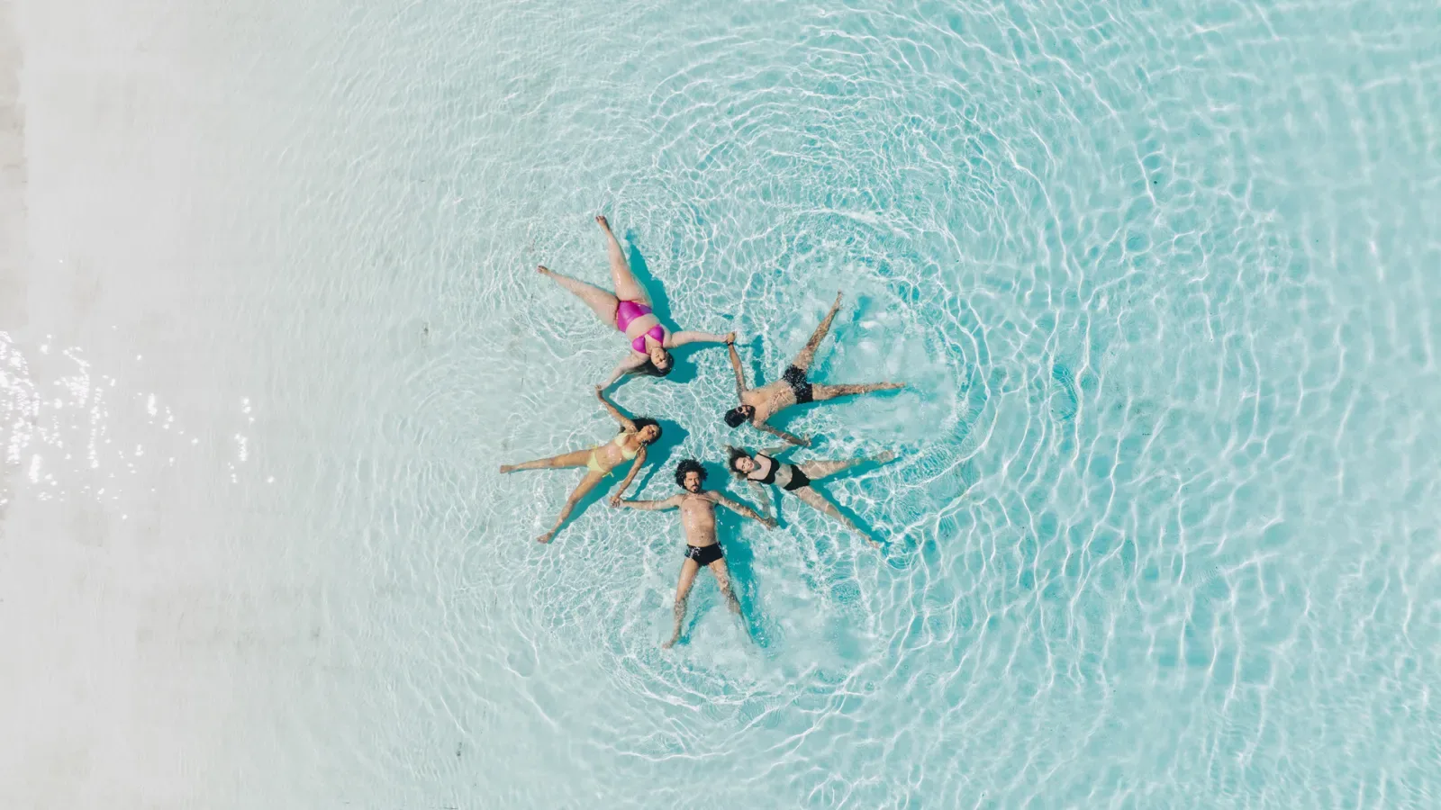 adults formando uma estrela deitados em uma psicina rasa com aguas cristalinas