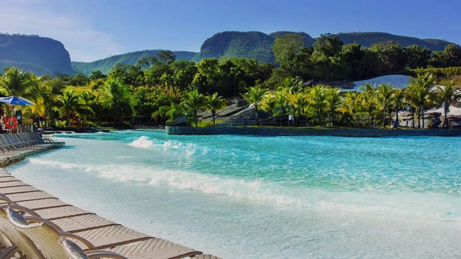 piscina de ondas azuis com cadeiras de praia e fundo de montanhas com mata nativa