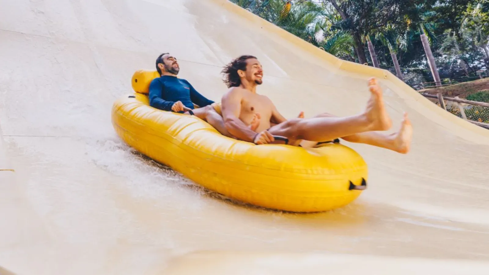 dois adultos homens, descendo uma boia amarela em um toboagua de um parque aquatico